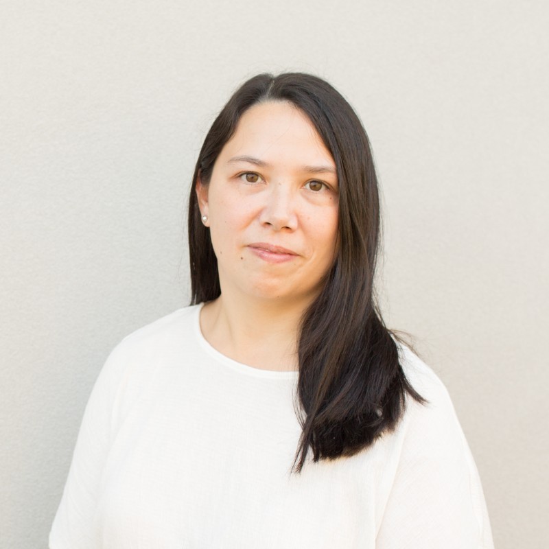 Professional headshot of Diana Racity with a serious expression against a light brown background.